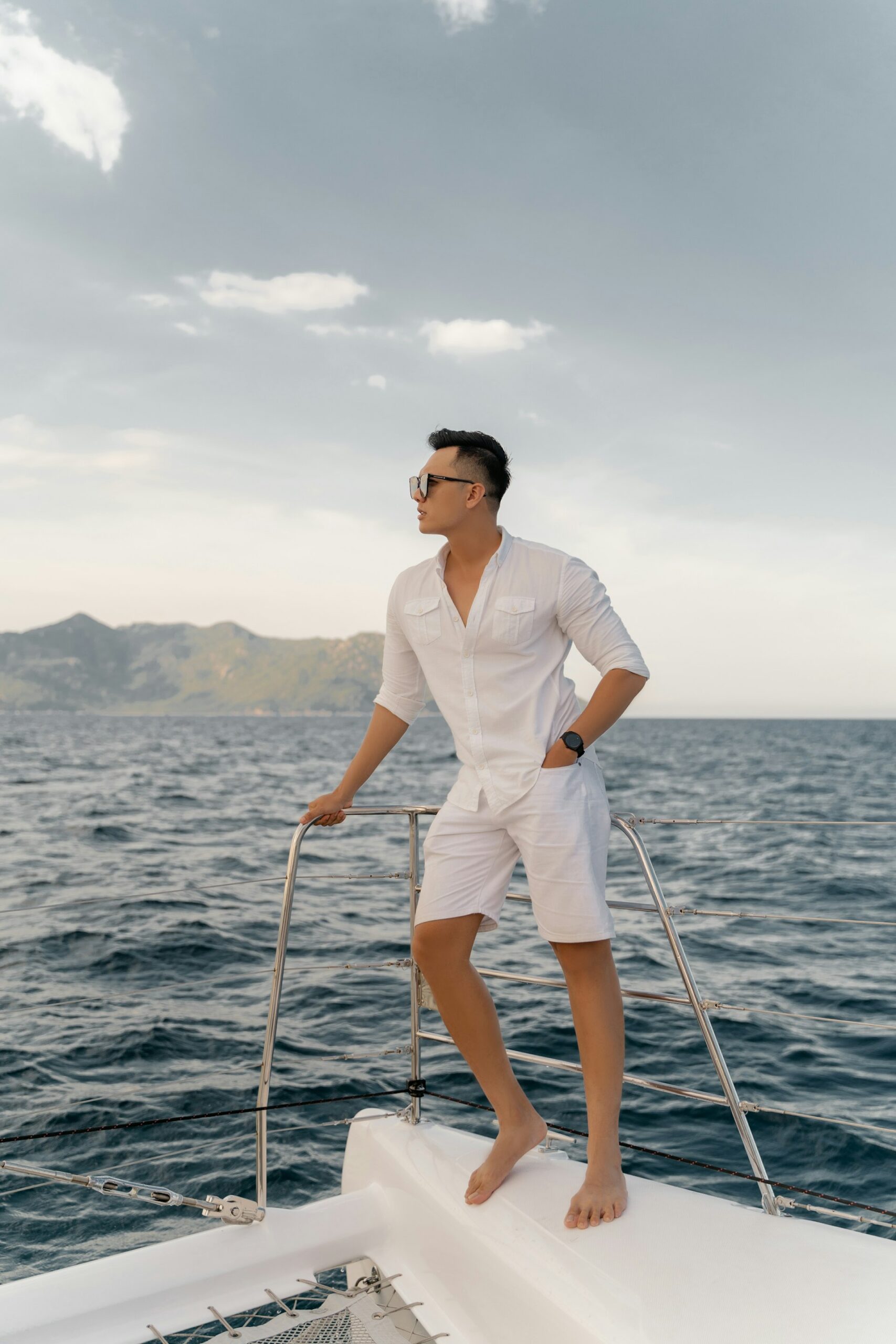 Man in a white polo, white shorts and sunglasses standing on the deck of a boat