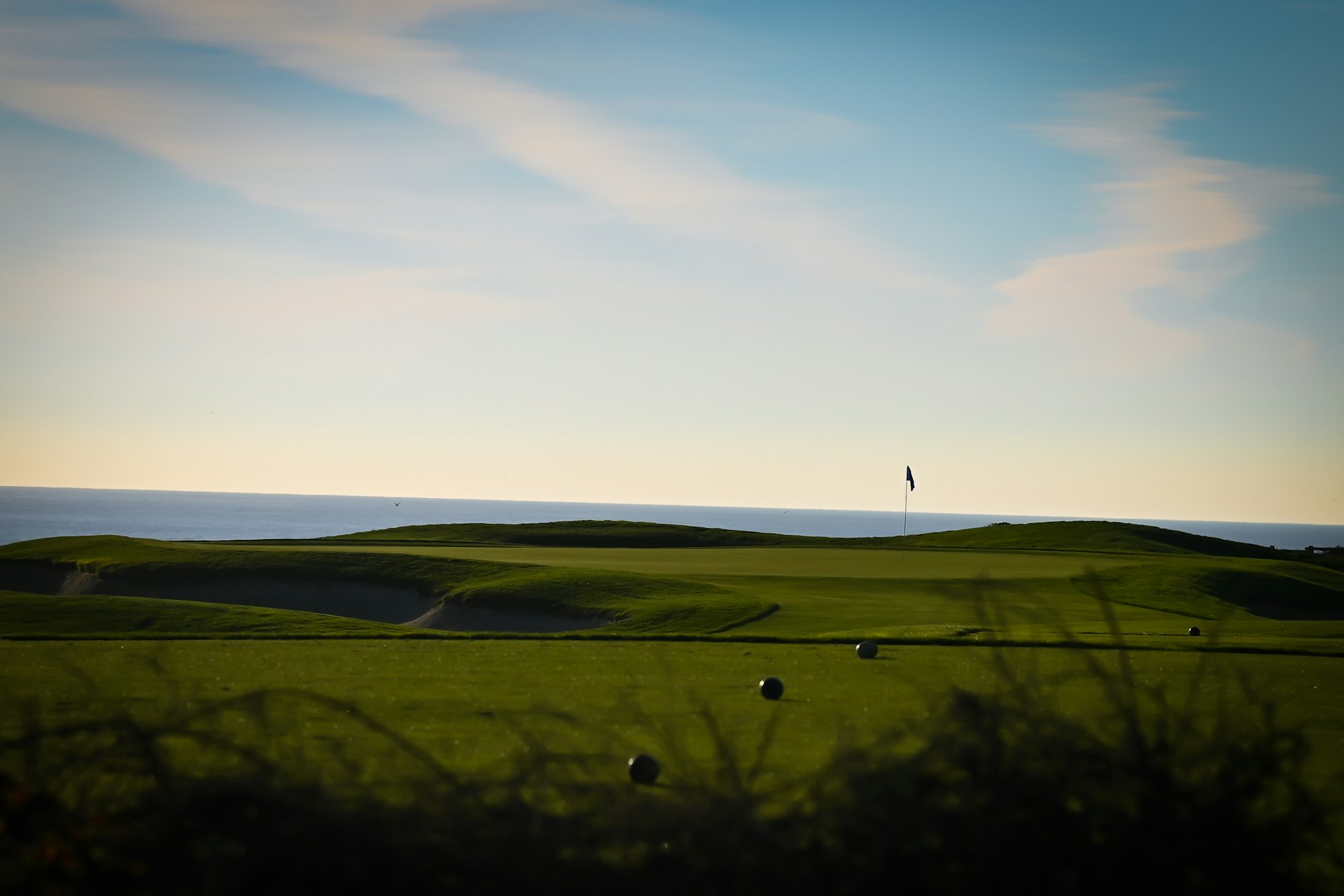 Golf green with a flagstick at the edge of the ocean in late afternoon light