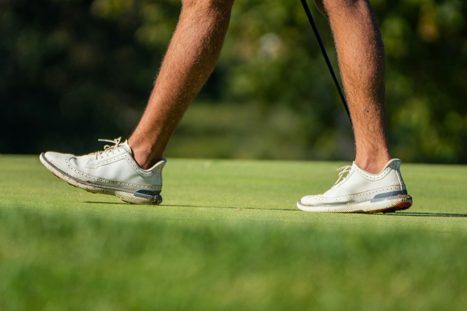 Golfer in light shoes walking across a sunlit green