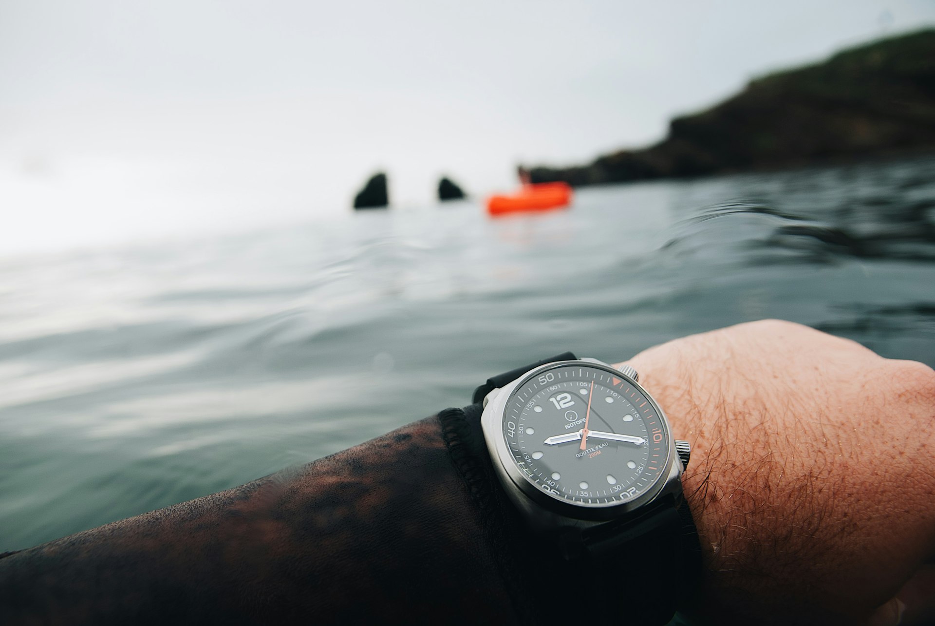 Wrist wearing a sport watch held over open water near a rocky coast